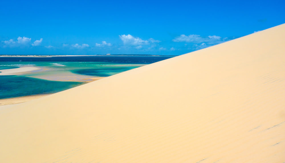 Weiße Sanddüne mit Blick auf das türkisfarbene Wasser und die Inselwelt des Bazaruto-Archipels vor der Küste Mosambiks.