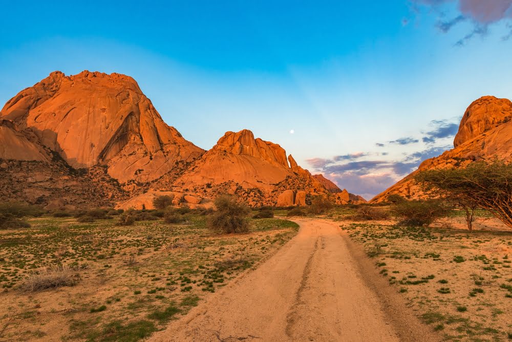 Spektakuläre Granitberge und Wüstenlandschaft im Damaraland in Namibia bei warmem Abendlicht mit unbefestigter Piste durch die Wildnis.